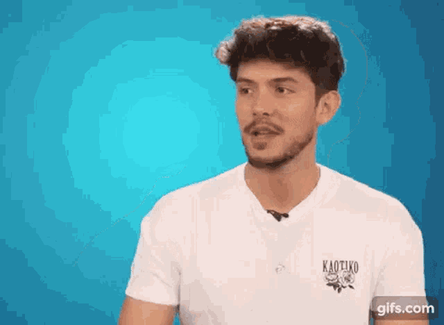 a man with a beard is wearing a white t-shirt with a kaotiko logo on it .