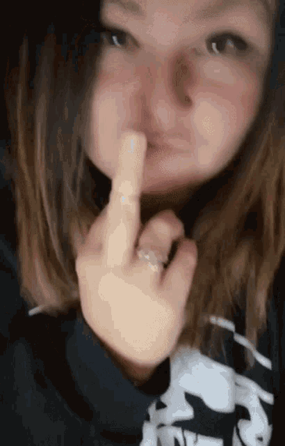 a woman with a ring on her finger is making a funny face and giving the middle finger .