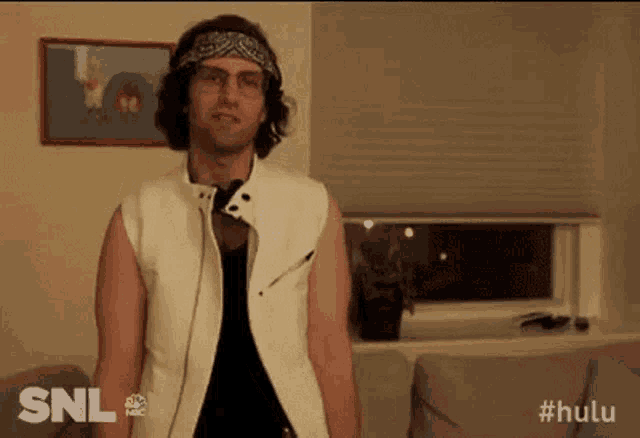 a man wearing a bandana and glasses is standing in front of a couch .