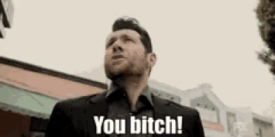 a man in a suit and tie is standing in front of a building and saying `` you bitch '' .