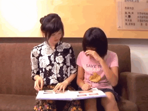 two girls are sitting on a couch and one has a shirt that says save the planet