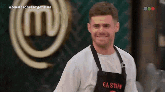 a man wearing an apron that says gaston smiles in front of a masterchef argentina logo