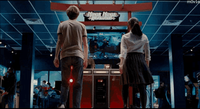 a man and a woman stand in front of a ninja ninja revolution arcade game