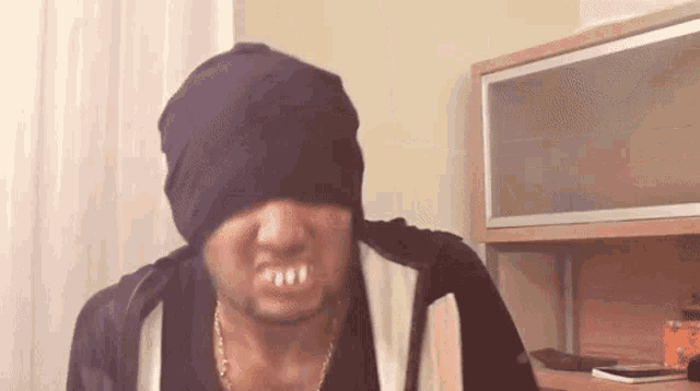 a man wearing a black beanie and a necklace is making a face