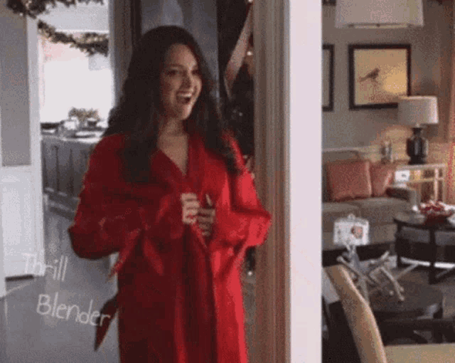 a woman in a red robe is standing in a living room with a sign that says thrill blender on it