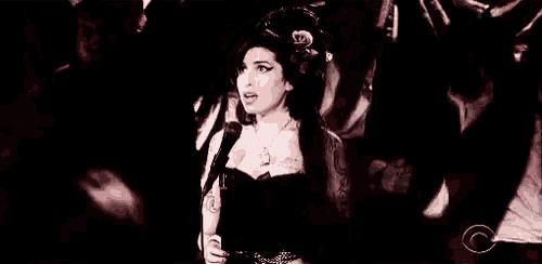 a woman is singing into a microphone on a stage in a black and white photo .