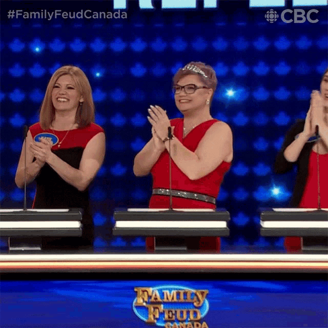 three women are clapping in front of a family feud canada logo