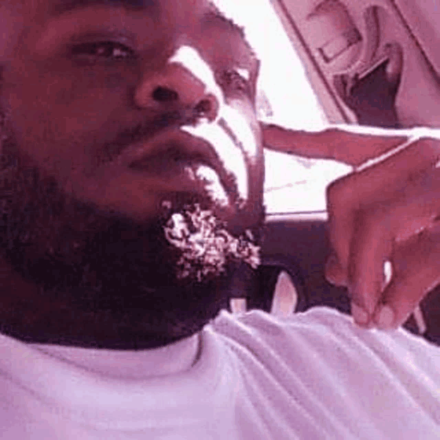 a man with a beard is taking a selfie in a car with his hand on his face .