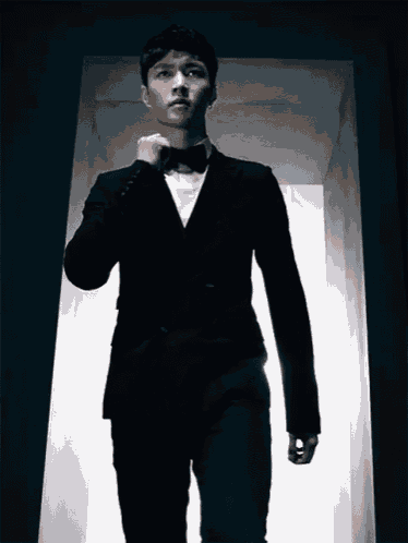 a man in a tuxedo and bow tie is walking through a doorway