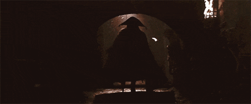 a silhouette of a person in a cape walking through a tunnel