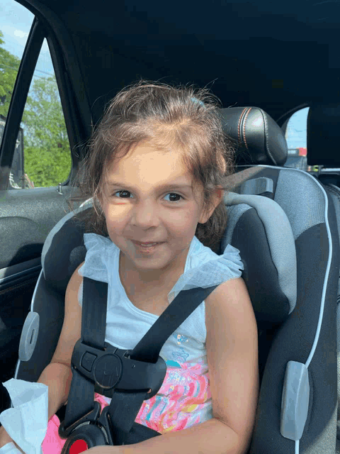 a little girl sits in a car seat and smiles for the camera