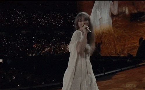a woman in a white dress singing into a microphone with the words ' cause it was never mine ' on the bottom right