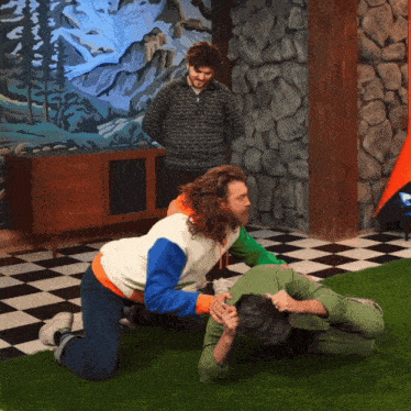 a man in a sweater with a pattern on it stands behind two men kneeling on the floor