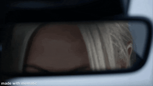 a woman is reflected in a rear view mirror while driving a car .