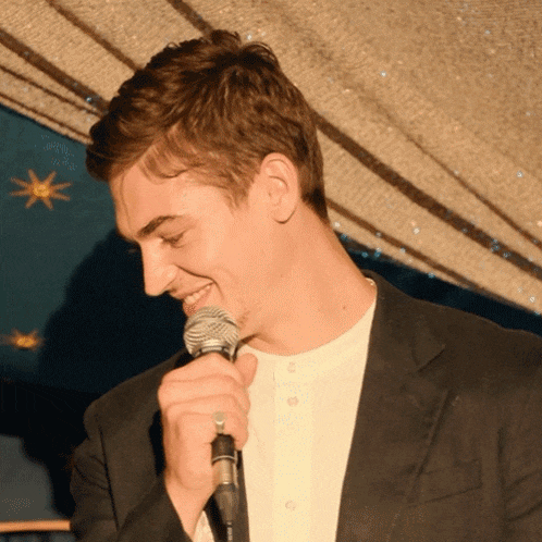 a man in a suit is singing into a microphone with a ring on his finger