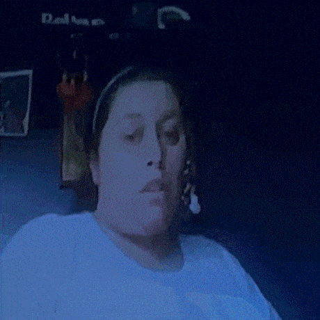 a woman wearing a headband and a white shirt is sitting in a dark room looking at the camera .