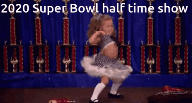 a little girl is dancing in front of trophies with the words 2020 super bowl half time show written above her