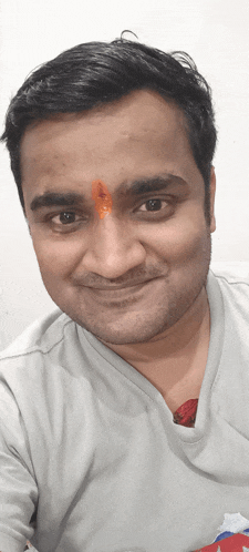 a man with a red dot on his forehead smiles