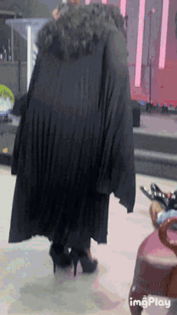 a woman in a black cape and high heels is walking on a stage with the words imgplay in the corner
