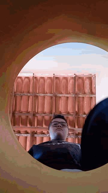 a man wearing glasses is looking down through a hole in the wall