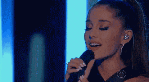 ariana grande is singing into a microphone with her eyes closed .