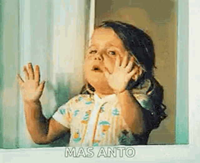a little girl is looking out of a window and waving .