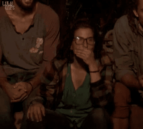 a woman with glasses is covering her mouth while sitting in a group of people ..