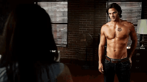 a shirtless man with a tattoo on his chest is standing in front of a window