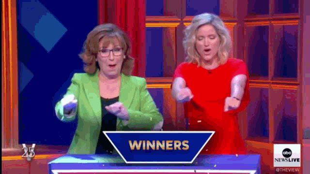 two women dancing in front of a sign that says " winners "