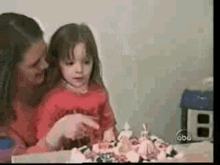 a woman and a little girl are sitting at a table looking at a cake .