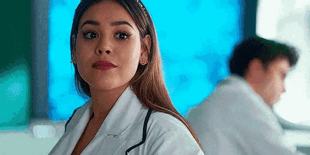 a woman in a lab coat with a stethoscope around her neck is sitting in front of a computer monitor .