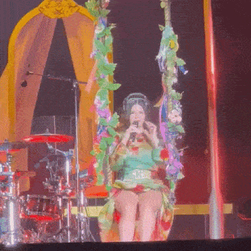 a woman is singing into a microphone while sitting on a swing on stage
