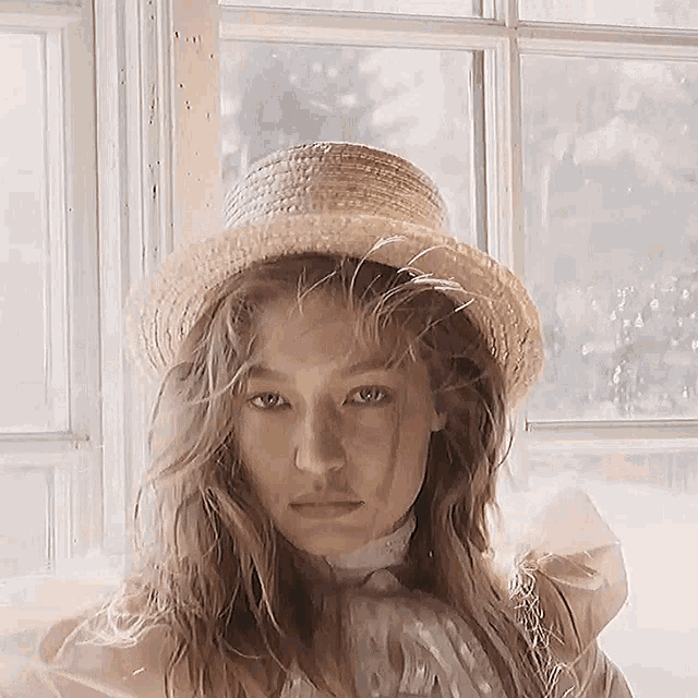 a woman wearing a straw hat and a pink dress is sitting in front of a window .