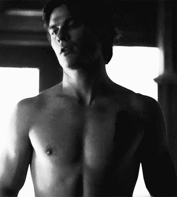 a man without a shirt is standing in front of a window .