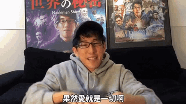 a man wearing glasses and a hat is sitting on a couch in front of a poster for naokiman shaw