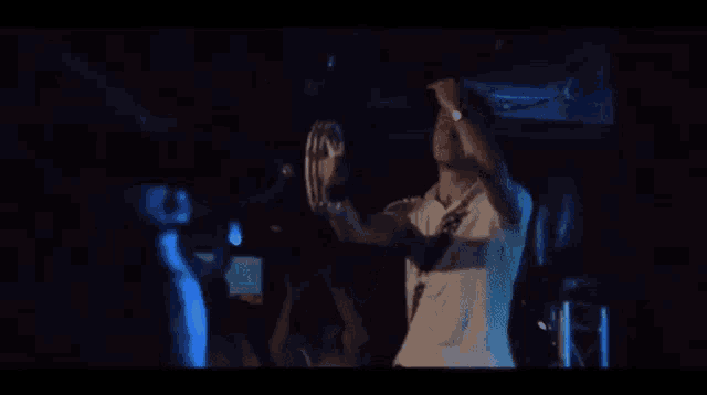 a man in a white shirt is standing in a dark room holding a drum .