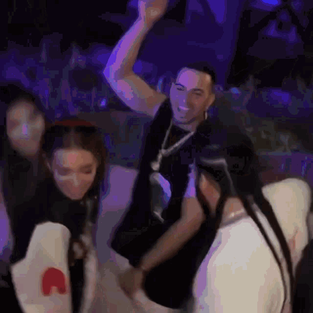 a group of people are dancing in a dark room with purple lights .