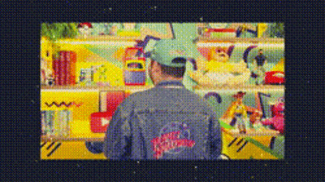 a man wearing a hat and a denim jacket is standing in front of a shelf full of toys .