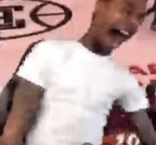a man in a white shirt is standing in front of a pink wall and laughing .