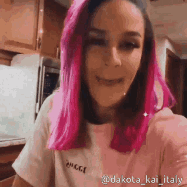 a woman with pink hair is taking a selfie in a kitchen .