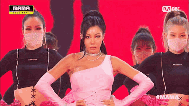 a woman in a pink dress is standing in front of a group of women wearing masks and gloves