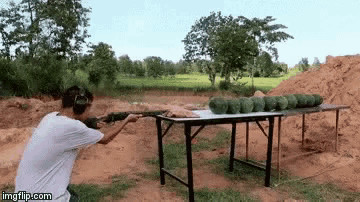 a man is aiming a gun at watermelons on a table ..
