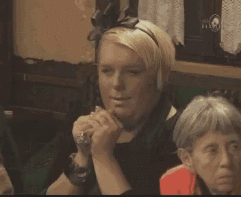a woman covering her face with her hands while sitting in a room with other people