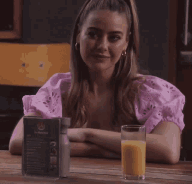 a woman is sitting at a table with a glass of orange juice