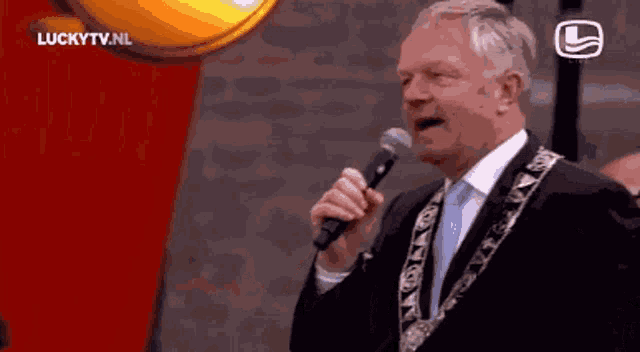 a man singing into a microphone with luckytv.nl written on the bottom right