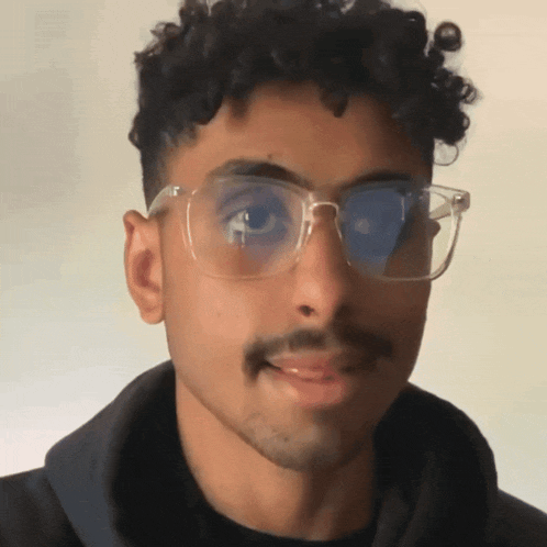 a man with curly hair wearing glasses and a black hoodie