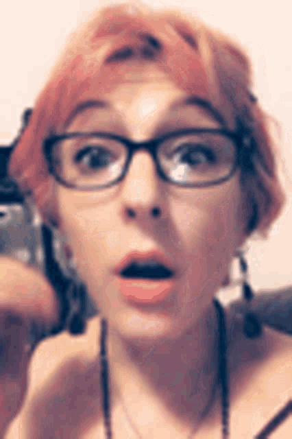 a woman wearing glasses and earrings is making a surprised face .