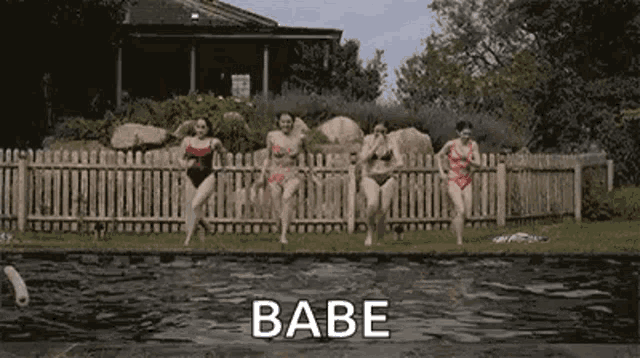 a group of women in swimsuits are dancing in front of a fence next to a pool .