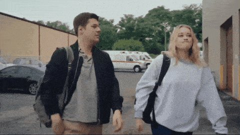a man and a woman walking down a street with an ambulance in the background