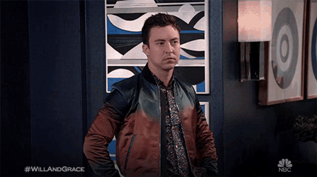 a man in a colorful jacket is standing in front of a wall with a nbc logo in the corner